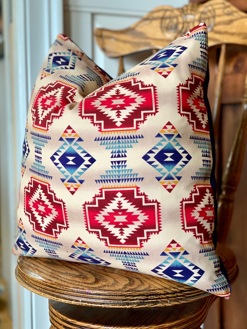 May include: A beige throw pillow with a geometric pattern in shades of red, blue, and yellow. The pattern is reminiscent of Native American designs.