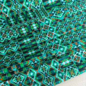 May include: Teal and green fabric with a geometric pattern. The pattern is made up of squares and triangles. The fabric has a textured surface.