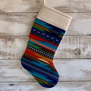 May include: A Christmas stocking with a colorful geometric pattern in shades of blue, green, orange, and brown. The stocking has a white cuff.