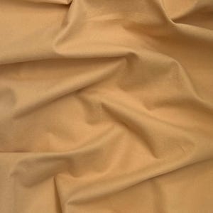 May include: Close-up of a folded piece of fabric in a warm, light tan color. The fabric has a soft, matte texture with subtle variations in tone, creating a sense of depth and dimension. The folds and creases add visual interest.