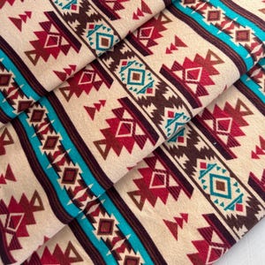 Könnte beinhalten: Stoff mit einem sich wiederholenden Muster aus geometrischen Formen in Braun-, Rot-, Türkis- und Weißtönen. Das Muster erinnert an indianische Designs.