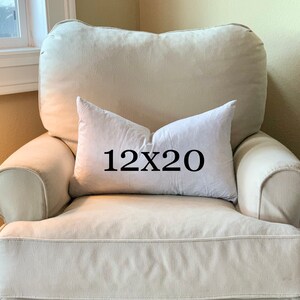 May include: A white throw pillow with black text that reads "12x20" on a cream-colored armchair.
