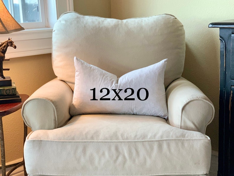 May include: A white throw pillow with black text that reads "12x20" on a cream-colored armchair.