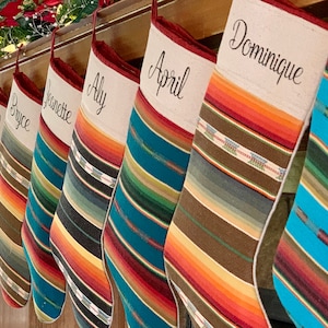 May include: A set of nine colorful striped stockings with names embroidered on them, including "Aly", "April", "Dominique", "Bryce", "Bill", "Jeanette", and "Ellie".