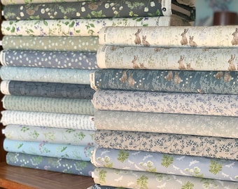May include: A stack of fabric featuring various nature-inspired patterns, including floral designs, bunnies, and dragonflies. The fabrics are in shades of blue, green, and beige.