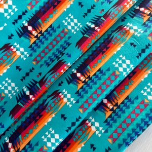 Puede incluir: Tela turquesa con un patrón geométrico colorido. El patrón presenta triángulos y diamantes de color naranja, rojo, blanco y azul.