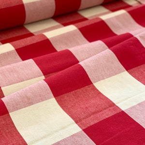 Könnte beinhalten: Rotes und weißes Gingham-Gewebe mit einem dezenten rosafarbenen Farbton. Der Stoff ist gefaltet und zeigt das Muster.