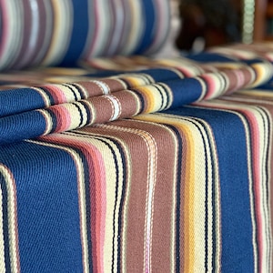 May include: Striped fabric in shades of navy blue, brown, cream, and pink. The fabric has a woven texture and is folded to show the pattern.