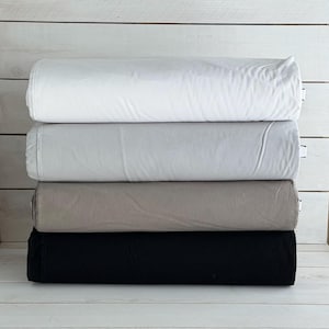 以下が含まれることがあります： 白、グレー、ベージュ、黒の4色の生地のロールが積み重ねられています。生地はきつく巻かれており、素材の質感がわかります。ロールはきちんと配置されており、さまざまな色のオプションが示されています。