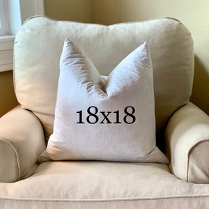 May include: A white pillow with the text "18x18" printed on it, sitting on a light beige armchair.