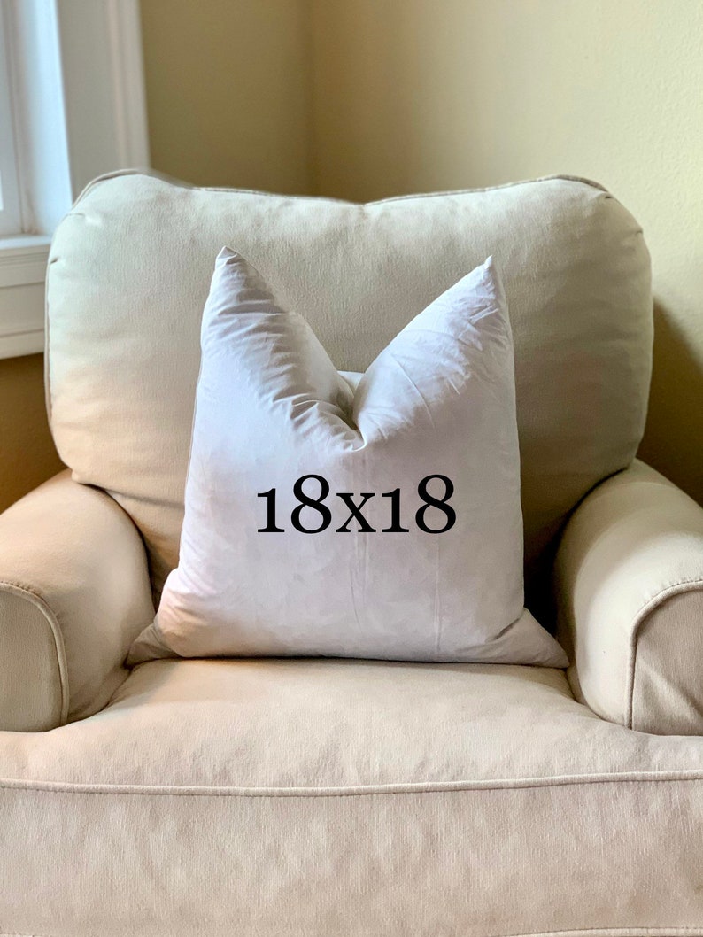 May include: A white pillow with the text "18x18" printed on it, sitting on a light beige armchair.