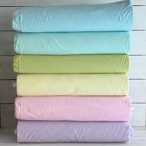Puede incluir: Una pila de seis sábanas dobladas en colores pastel: azul claro, verde menta, verde lima, amarillo pálido, rosa y lavanda. Las sábanas están cuidadosamente dobladas y apiladas, mostrando la variedad de colores.