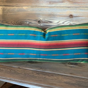 May include: A teal, red, orange, yellow, and green striped lumbar pillow. The pillow is on a wooden surface.
