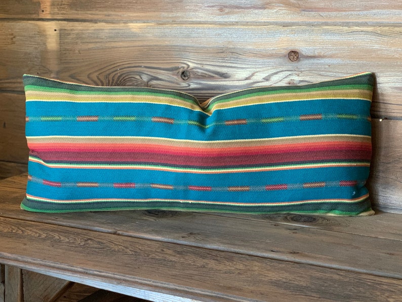 May include: A teal, red, orange, yellow, and green striped lumbar pillow. The pillow is on a wooden surface.