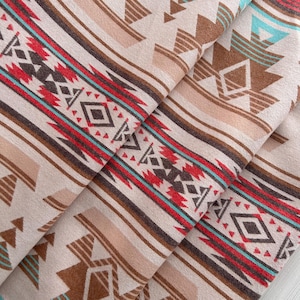 Pode incluir: Um tecido bege com um padrão geométrico repetitivo em marrom, vermelho e turquesa. O padrão lembra os desenhos dos nativos americanos.