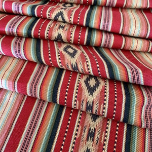 May include: Close-up of a red, black and cream striped fabric with a geometric pattern. The fabric is folded in layers, showing the different colours and patterns.