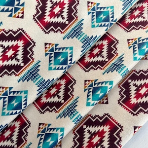 Puede incluir: Una tela blanca con un patrón geométrico repetitivo en tonos de rojo, azul, turquesa y marrón. El patrón recuerda a los diseños de los nativos americanos.