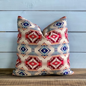 May include: A decorative throw pillow with a geometric pattern in shades of red, blue, and yellow on a cream background.