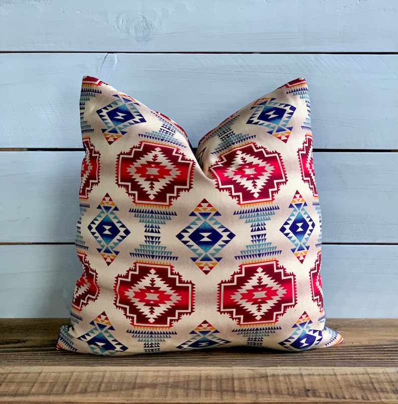 May include: A decorative throw pillow with a geometric pattern in shades of red, blue, and yellow on a cream background.