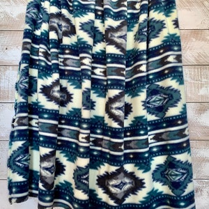 May include: A soft, plush blanket with a white background and a blue, green, and gray geometric pattern. The blanket is folded and has a fringed edge.