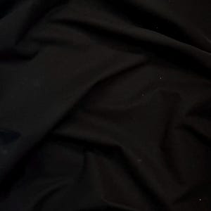 May include: A close-up shot of a black fabric with soft folds and subtle highlights. The material appears to be smooth and possibly a lightweight textile, with a slightly glossy sheen. The dark color suggests a versatile material suitable for various apparel or craft projects.