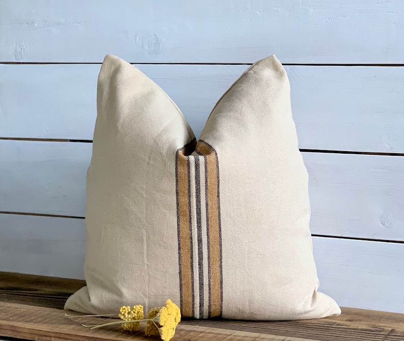 May include: A cream-colored pillow with brown and tan stripes down the center. The pillow is sitting on a wooden surface.