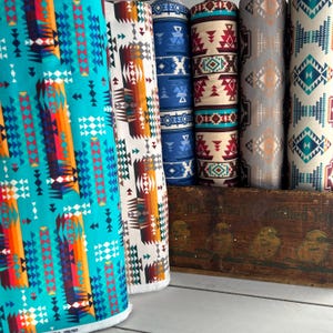 May include: Five rolls of fabric with geometric patterns in shades of blue, red, orange, white, and gray. The fabric is arranged on a wooden crate with the text "Air Cushioned Yo"
