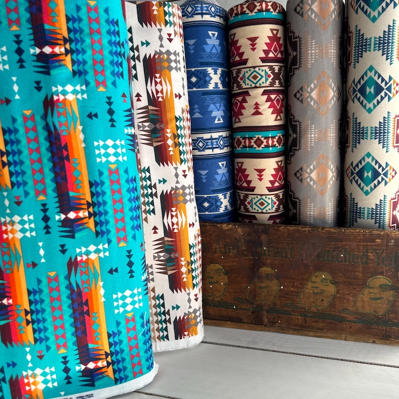 May include: Five rolls of fabric with geometric patterns in shades of blue, red, orange, white, and gray. The fabric is arranged on a wooden crate with the text "Air Cushioned Yo"