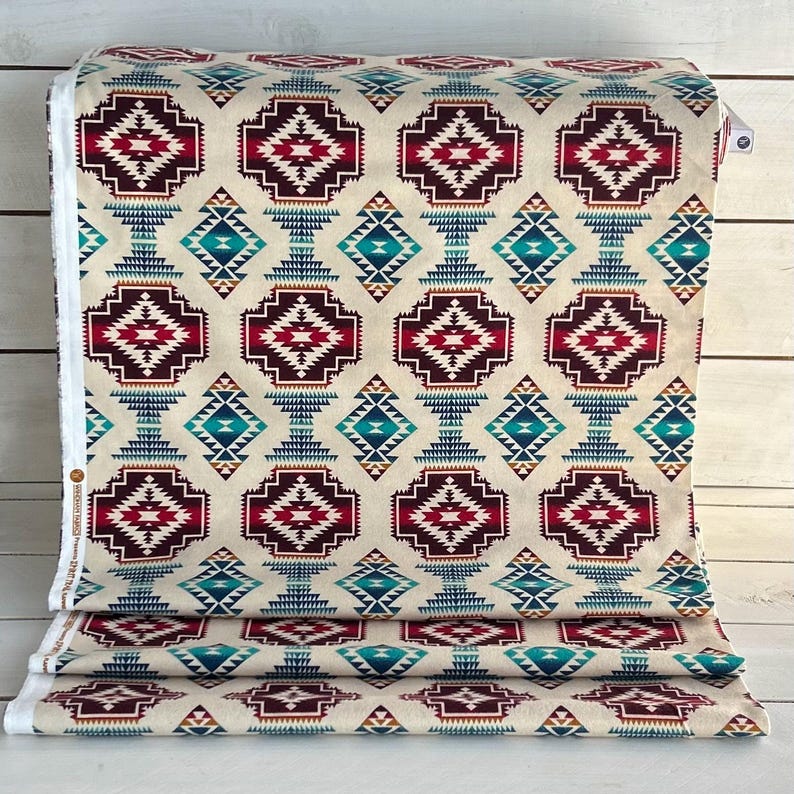 May include: Beige fabric with a repeating geometric pattern in shades of red, blue, and brown. The pattern features a large diamond shape with smaller diamond shapes inside. The fabric is folded in thirds.