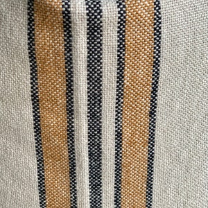 May include: Close-up of a woven fabric with alternating stripes of beige and black. The fabric has a textured, slightly rough surface.