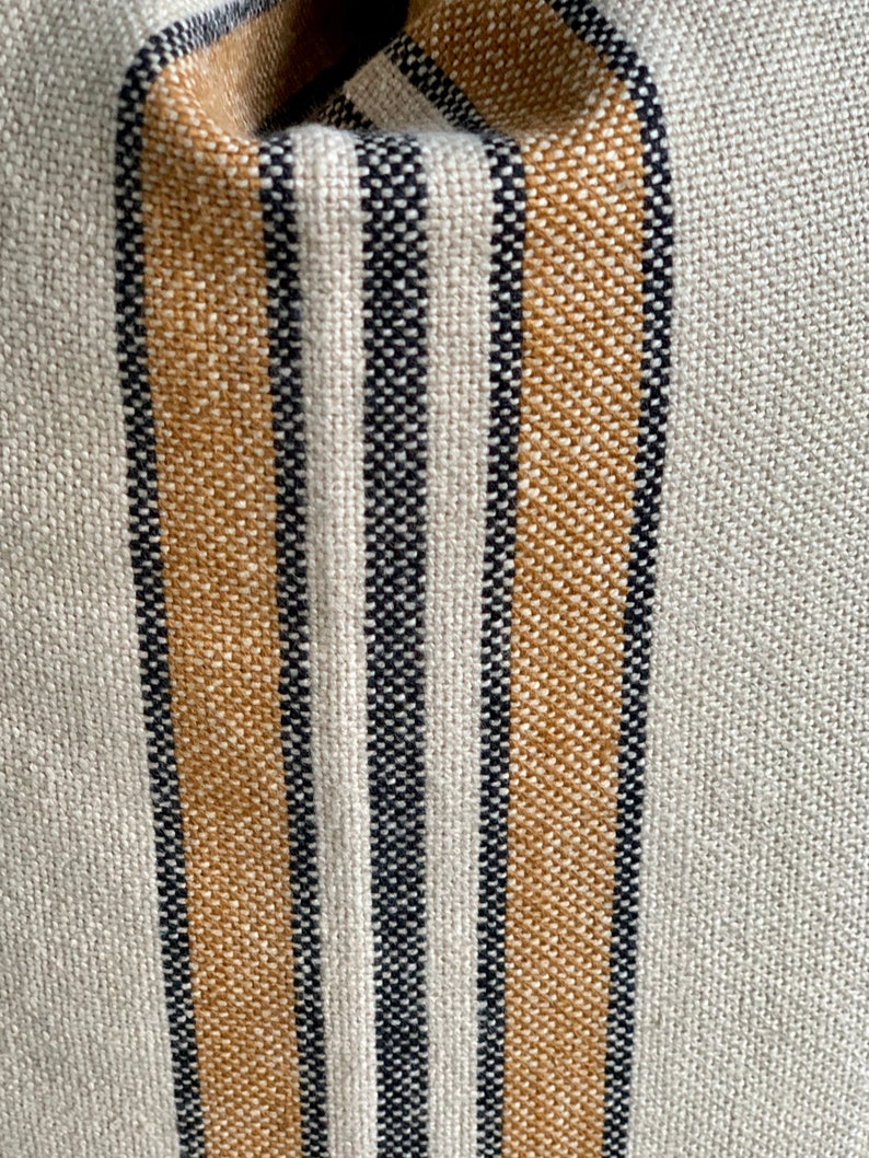 May include: Close-up of a woven fabric with alternating stripes of beige and black. The fabric has a textured, slightly rough surface.