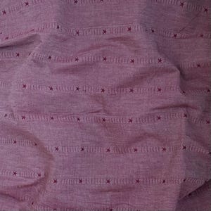 May include: Close-up of a textured, crumpled fabric in a deep mauve colour. The fabric features horizontal stripes with small, dark red star-shaped accents. The overall appearance suggests a textile suitable for clothing or home decor.