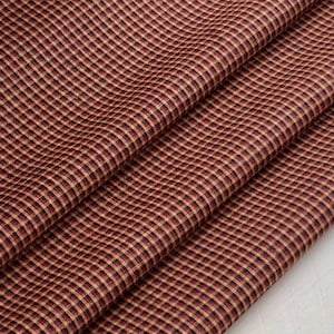 Op de afbeelding: Rode en bruine gingham stof met een fijn geruit patroon. De stof is gevouwen en gedrapeerd, waardoor de textuur en kleur worden getoond.