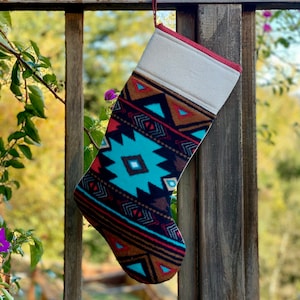May include: A Christmas stocking with a colorful geometric pattern in shades of brown, red, blue, and white. The stocking is hanging on a wooden railing.