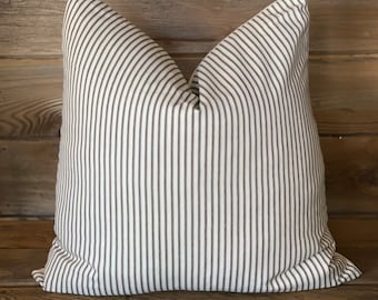 May include: A white pillow with thin black stripes. The pillow is sitting on a wooden surface.