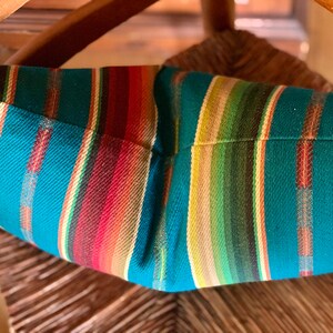 May include: A teal, red, green, and beige striped throw pillow with a woven texture.