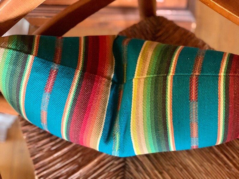 May include: A teal, red, green, and beige striped throw pillow with a woven texture.