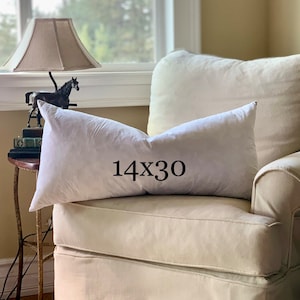 May include: A white armchair with a white pillow on top. The pillow has the text "14x30" printed on it.