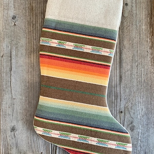 May include: A striped Christmas stocking with a brown, orange, red, green, and blue pattern. The stocking is made of a woven fabric and has a white cuff.