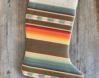 Könnte beinhalten: Ein gestreifter Weihnachtsstrumpf mit einem braunen, orangen, roten, grünen und blauen Muster. Der Strumpf ist aus gewebtem Stoff und hat einen weißen Bund.