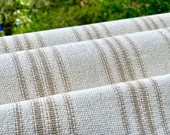 May include: Close-up of a white linen fabric with brown stripes. The fabric is folded in thirds, showing the texture and weave of the material.