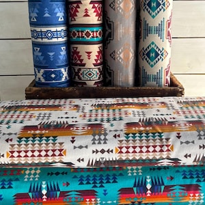 May include: Four rolls of fabric with geometric patterns in shades of blue, red, white, and brown. The fabric is stacked on a wooden crate. The fabric is folded and has a geometric pattern.