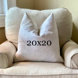 May include: A white pillow with the text "20x20" printed on it, sitting on a light beige armchair.