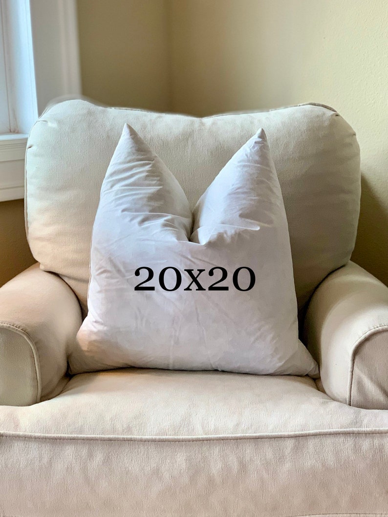 May include: A white pillow with the text "20x20" printed on it, sitting on a light beige armchair.
