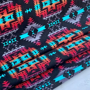 Peut inclure: Tissu noir avec un motif géométrique coloré. Le motif présente des teintes turquoise, orange, rouge et violette. Le tissu est plié en trois.