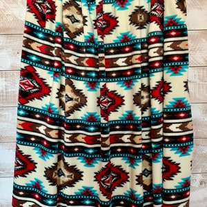 Peut inclure: Une couverture douce et moelleuse avec un motif d'inspiration sud-ouest présentant des formes géométriques dans des tons de rouge, marron, turquoise et blanc.