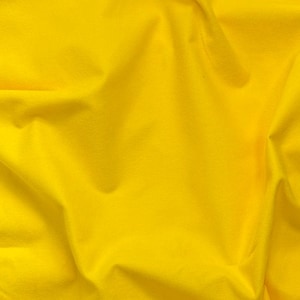 May include: Close-up of a bright yellow fabric with visible folds and textures. The fabric appears soft and opaque, with variations in light and shadow across its surface. The overall impression is of a smooth, flowing material.