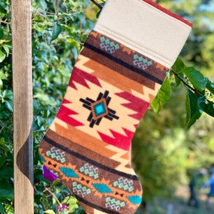 May include: A red, brown, and beige stocking with a geometric pattern and turquoise accents. The stocking is made of fleece and has a white cuff.