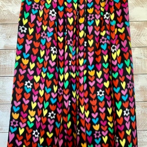 May include: Black fleece fabric with a repeating pattern of colorful hearts and white flowers.