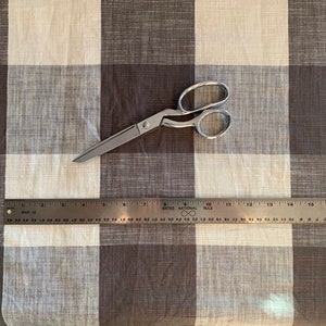 May include: A brown and white checkered fabric with a pair of silver scissors and a ruler. The ruler is marked with inches and has the text "Bates National Rule" printed on it.